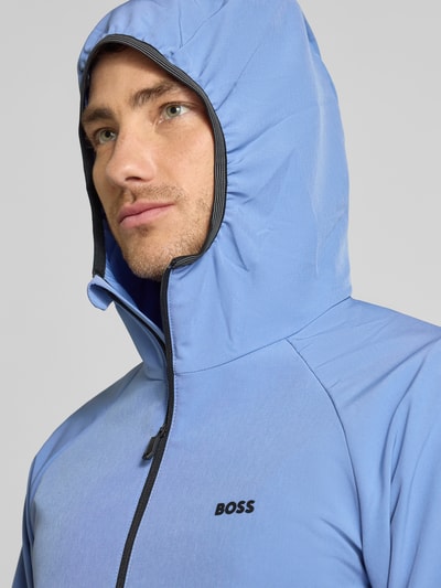 Männermodel trägt Regular Fit functioneel jack uit waterdicht materiaal model 'L_COMMUTER' van BOSS in effen kleuren met lange mouw, labelprint, capuchon en ritssluiting, warmte-isolatie, zij-ritszakken, nahaufnahme bovenlichaam.