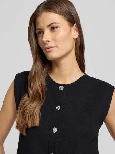 Frauenmodel trägt Regular Fit Strickjacke aus Viskose-Mix Modell 'GOLD' von Vero Moda, schwarz, Strickoptik, Nahaufnahme Oberkörper.