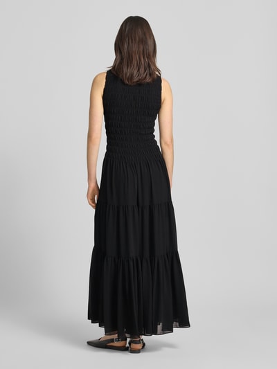 Frauenmodel trägt Maxikleid mit Smok-Details und Volantsaum von MICHAEL Michael Kors, in Schwarz, taillierter Schnitt, Rückenlänge 141 cm, Brustweite 31 cm, Ganzkörperansicht Rückansicht.