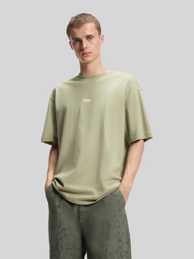 Männermodel trägt Relaxed Fit T-Shirts aus reiner Baumwolle von HUGO Blue in hellem Grün, glatte Textur, Ganzkörperansicht von vorne.