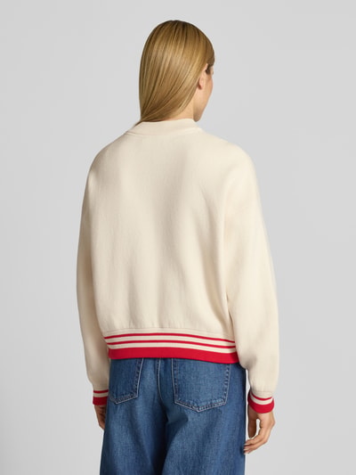 Frauenmodel trägt Oversized Bomberjacke aus Baumwoll-Mix mit Woll-Anteil Modell 'ICONIC A' von Armedangels, cremefarben, rote Rippbündchen, unifarbenes Design, College-Kragen, Ganzkörperansicht Rückansicht.