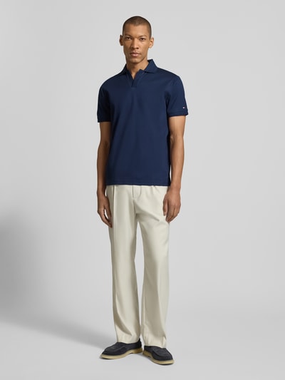 Männermodel trägt Regular Fit Poloshirt aus reiner Baumwolle von Tommy Hilfiger in Dunkelblau, unifarben, Logo-Detail, Ganzkörperansicht von vorne.