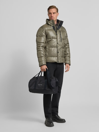 Męski model prezentuje Weekender mit Label-Stitching od CK Calvin Klein, czarny materiał, srebrne zamki, zdjęcie całościowe z przodu. Produkt posiada główną kieszeń z zamkiem, uchwyty, odpinany pasek na ramię, wewnętrzną kieszeń oraz wymiary: szerokość 45 cm, długość 24 cm, głębokość 22 cm, pasek 90 cm.