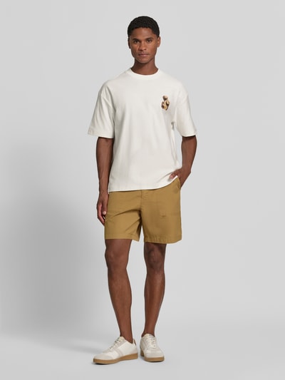 Männermodel trägt Regular Fit T-Shirt aus reiner Baumwolle Modell 'Detzi' von HUGO in Weiß mit braunen Shorts, Ganzkörperansicht von vorne, Herren T-Shirt von HUGO