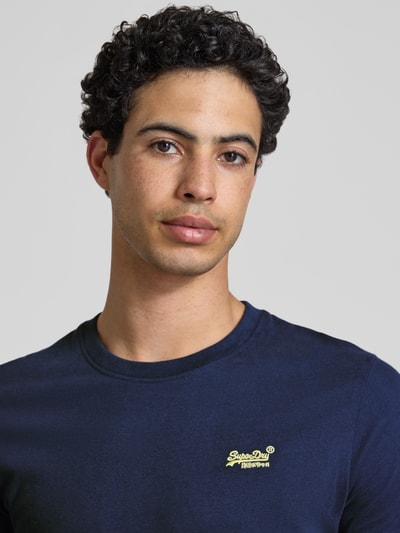 Männermodel trägt Regular Fit T-Shirt mit Logo-Stitching von Superdry aus reiner Baumwolle, Rundhalsausschnitt, Nahaufnahme Oberkörper.