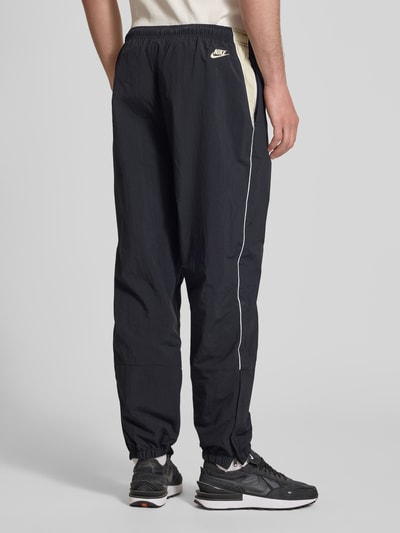 Männermodel trägt Trainingshose mit Logo und elastischem Bund von Nike, Relaxed-Fit, elastische Beinabschlüsse, Ganzkörperansicht Rückansicht. Innenbeinlänge bei Größe M: 76 cm.