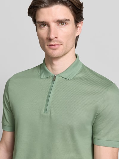 Männermodel trägt Regular Fit Poloshirt aus Baumwoll-Lyocell-Mix Modell 'H-PARAS 70' von BOSS in grün, Piqué-Struktur, Nahaufnahme Oberkörper.