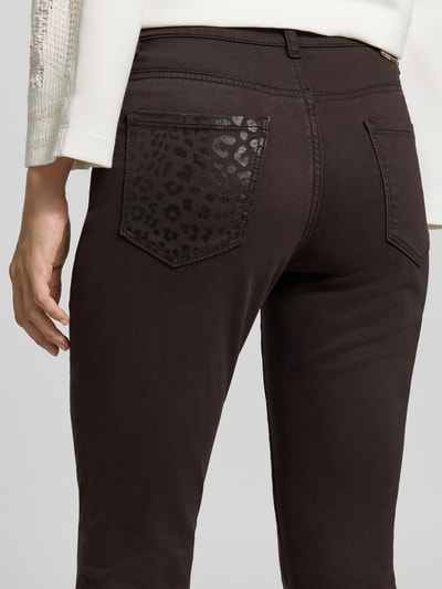 Frauenmodel trägt Slim Fit Jeans mit Lyocell-Anteil von Marc Cain, dunkler Braunton, Leo-Muster auf Gesäßtasche, Detailaufnahme Rückansicht, elastischer Material-Mix, 5-Pocket-Design, 7/8-Länge.