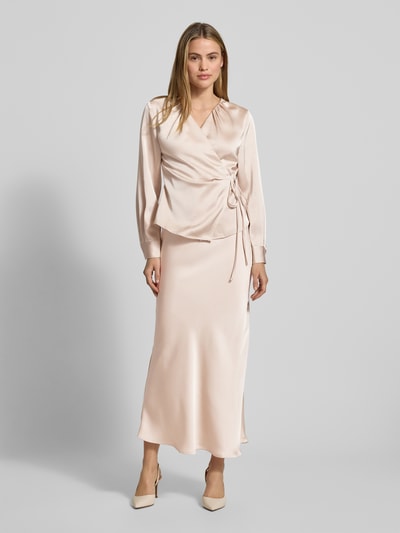 Frauenmodel trägt Wickelbluse aus Satin Modell 'Caprina' von Neo Noir in zartem Beige, taillierter Schnitt, V-Ausschnitt, fließende Textur, Ganzkörperansicht von vorne.
