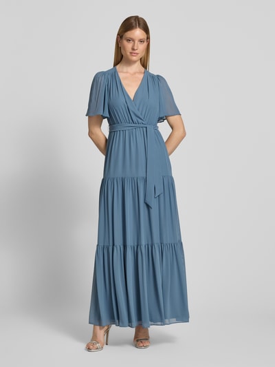 Frauenmodel trägt Abendkleid mit V-Ausschnitt und Bindegürtel von Christian Berg Cocktail aus Chiffon in Blau, Stufen-Look, Maxikleid, A-Linie, Ganzkörperansicht von vorne. Rückenlänge bei Größe 36: 151 cm, Brustweite: 41 cm, Ärmellänge: 30 cm.
