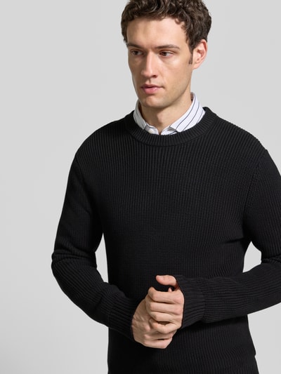 Männermodel trägt Regular Fit Strickpullover aus reiner Baumwolle von MCNEAL, schwarze Farbe, strukturierte Oberfläche, Nahaufnahme Oberkörper. Rückenlänge 73 cm, Ärmellänge 53 cm, Rundhalsausschnitt, elastische Abschlüsse.