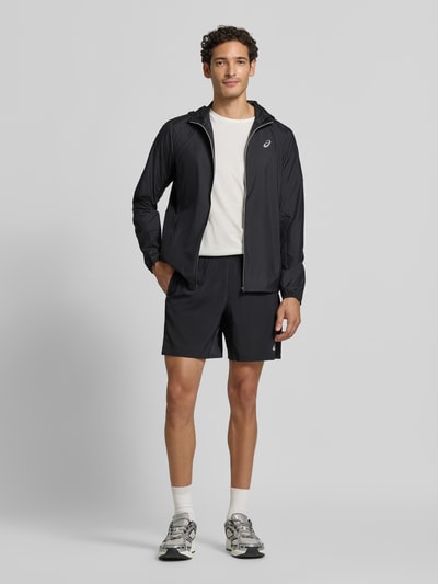 Männermodel trägt schwarze Regular Fit Trainingsjacke mit Logo-Print Modell 'Core' von ASICS TIGER, glatte Oberfläche, Ganzkörperansicht von vorne.