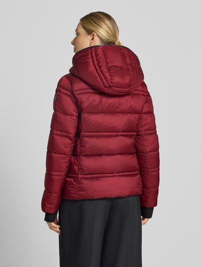 Frauenmodel trägt Steppjacke mit Kapuze und Reißverschlusstaschen von MICHAEL Michael Kors in Rot, glatte Oberfläche, Ganzkörperansicht Rückansicht. Modell 'PACKABLE WITH BIB', gerader Schnitt, Steppnähte, Kapuze mit Kordelstoppern, Reißverschluss, seitliche Reißverschlusstaschen, elastische Saumabschlüsse mit Daumenloch. Rückenlänge bei Größe S: 63 cm, Schulterbreite: 43 cm, Brustweite: 53 cm, Ärmellänge: 68 cm.
