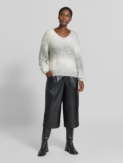 Kobieta modelka nosi sweter z dzianiny Strickpullover aus Effektgarn mit V-Ausschnitt od Apricot, Mieszanka materiałów z dodatkiem wełny, krój regular fit, efektowna przędza, dekolt w serek, długość tyłu w rozmiarze S 46 cm, długość rękawów w rozmiarze S 49 cm, widok na całą sylwetkę z przodu.