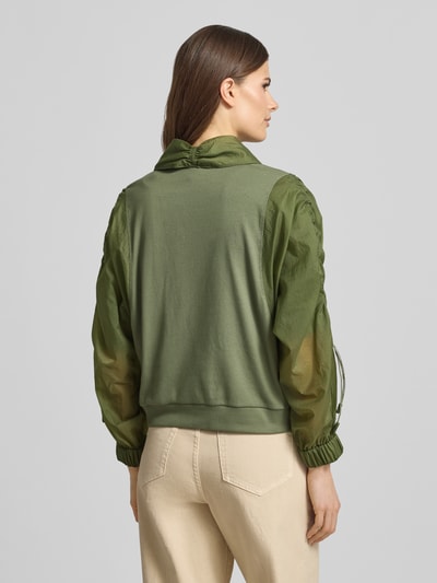 Modelka nosi Relaxed Fit Leichte Jacke im Material-Mix von Marc Cain, efekt: jednolity kolor, krój relaxed fit, krótki szalowy kołnierz, marszczenie, zapięcie: zakryta listwa guzikowa, rękaw o dł. 3/4, wykończenie materiału: satyna, szyfon, materiał: mieszanka bawełny, zielone odcienie, mieszane faktury. Widok całej sylwetki z tyłu.