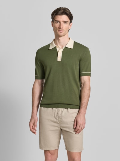 Męski model nosi Slim Fit Poloshirt mit Logo-Stitching od Gant w kolorze zielonym z beżowym kołnierzykiem, bawełna-modal, krój slim fit, długość tyłu w rozmiarze M: 69 cm, widok całej sylwetki z przodu.