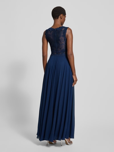 Frauenmodel trägt Abendkleid mit floralen Stickereien von Mascara in Dunkelblau, taillierte Passform, Rückenreißverschluss, mehrlagiger Rockteil, transparente Einsätze, Rückenlänge bei Größe 36: 153 cm, Brustweite: 36 cm, Ganzkörperansicht Rückansicht.