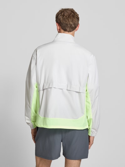 Männermodel trägt Regular Fit Jacke in Stehkragen Modell 'Fast Days' von New Balance, Farbkontrast Weiß und Neon-Grün, elastische Ärmelabschlüsse, Tunnelzug im Bund, Rückenlänge 68 cm, Eingrifftaschen mit Reißverschluss, Ganzkörperansicht Rückansicht.