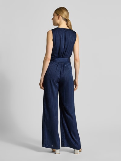 Frauenmodel trägt Jumpsuit mit Strukturmuster Modell 'Telma' von SUNCOO PARIS in Dunkelblau, tailliert, ärmellos, Stoffband, Ganzkörperansicht Rückansicht.