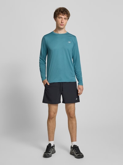 Männermodel trägt Funktionsshirt mit Rundhalsausschnitt und Logo von New Balance in Türkis, Regular Fit, Longsleeve, Ganzkörperansicht von vorne.