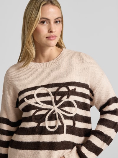 Modelka nosi Strickpullover im Allover-Look mit Rundhalsausschnitt von MORE & MORE, beżowo-brązowe pasy, tekstura dzianiny, relaxed fit, długość tyłu 53 cm, długość rękawa 53 cm, zbliżenie na górną część ciała.