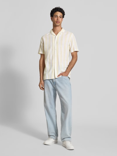 Männermodel trägt Regular Fit Leinenhemd aus Baumwoll-Leinen-Mix Modell 'CAIDEN' von Only & Sons mit gelb-weißen Streifenmuster, Kurzarm, Resortkragen, durchgehender Knopfleiste; Ganzkörperansicht von vorne.