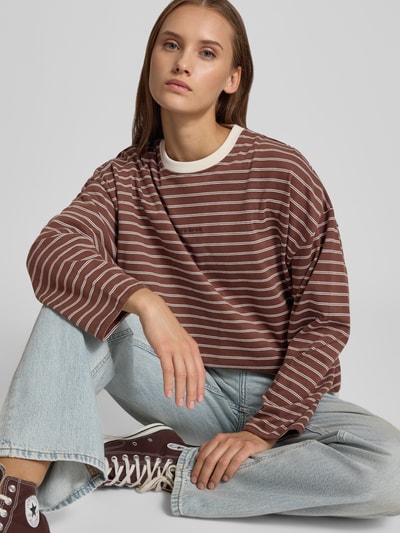 Vrouwenmodel draagt shirt met lange mouwen van OH APRIL in bruin met witte strepen, puur katoen, losse pasvorm, ronde hals, geborduurd label, ruglengte bij maat S: 53 cm, vooraanzicht fullbody.