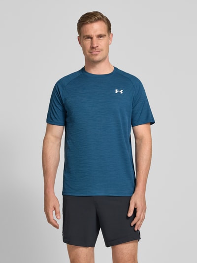 Męski model nosi T-Shirt mit Label-Print Modell 'Tech' von Under Armour, prosty krój, okrągły dekolt, długość tyłu w rozmiarze M: 75 cm, kolor niebieski z białym nadrukiem z logo, tekstura gładka, Ganzkörperansicht von vorne.