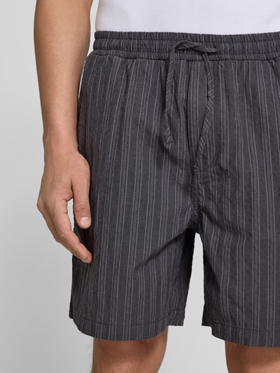 Männermodel trägt Shorts mit Stretch-Anteil von Forét in Dunkelgrau mit weißen Streifen, Baumwoll-Elasthan-Mix, Nahaufnahme Oberkörper.
