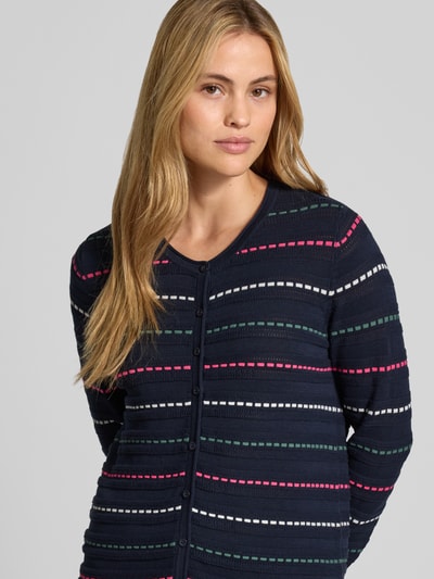 Frauenmodel trägt Cardigan aus reiner Baumwolle von Christian Berg Woman, dunkelblau mit bunten Streifen, Nahaufnahme Oberkörper. Eng anliegende Passform, Rundhalsausschnitt, durchgehende Knopfleiste, Rückenlänge 62 cm, Ärmellänge 72 cm.