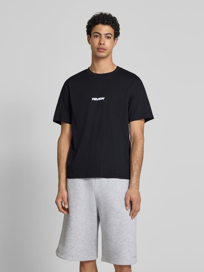 Męskimodel nosi T-Shirt mit Logo und Rundhalsausschnitt od REVIEW, męski t-shirt z bawełny, krój relaxed fit, okrągły dekolt, długość tyłu 68 cm, Ganzkörperansicht von vorne.