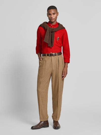 Męski model nosi Custom Fit Freizeithemd mit Motiv-Stitching od Polo Ralph Lauren, czysta bawełna, kołnierz button-down, zapięcie na guziki, kieszeń na piersi, haft motywu, długość pleców w rozmiarze M: 79 cm, szerokość ramion w rozmiarze M: 43 cm, długość rękawa w rozmiarze M: 64 cm, czerwony, brązowe dodatki, widok całej sylwetki z przodu.