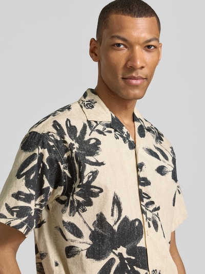 Männermodel trägt entspannt geschnittenes Relaxed Fit Freizeithemd mit Reverskragen Modell 'BLAVENICE' von Jack & Jones Premium, Bio-Baumwoll-Mix, cremefarben mit schwarzem Blumenmuster, weiche Textur, Nahaufnahme Oberkörper.
