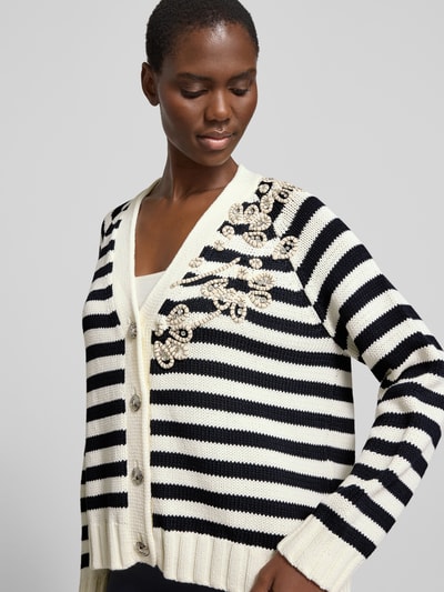 Frauenmodel trägt Relaxed Fit Cardigan mit Ziersteinbesatz von Liu Jo White, Baumwoll-Mix, Strick-Optik, V-Ausschnitt, Knopfleiste, floraler Zierbesatz, elastische Abschlüsse, gestreiftes Schwarz-Weiß-Design, Nahaufnahme Oberkörper.