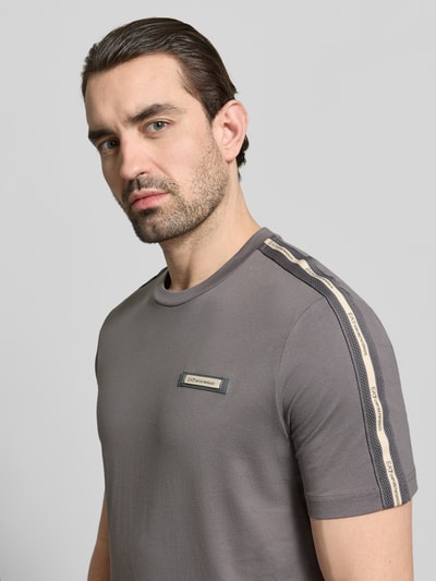 Mężczyznamodel nosi Regular Fit T-Shirt mit Logo-Patch od EA7 Emporio Armani z bawełny, okrągły dekolt, krój regular fit, naszywka z logo, długość tyłu w rozmiarze M: 52 cm, szara kolorystyka, tekstura gładka, zbliżenie na górną część ciała