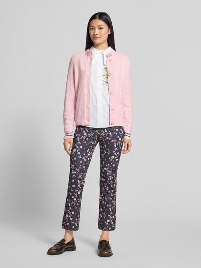 Modelka nosi Regular Fit Cardigan aus Baumwoll-Mix in Strick-Optik von Marc Cain, różowy, okrągły dekolt, listwa guzikowa, Imitacja dzianiny, długość tyłu 56 cm, długość rękawa 62 cm, mieszanka bawełny, widoczne faktury dzianiny, pełne spodnie w kwiaty, widok całej sylwetki z przodu.