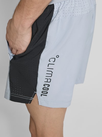 Männermodel trägt Regular Fit Sport-Shorts aus schnelltrocknendem Material von adidas Training, Mehrfarbig, perforierte Einsätze, seitliche Eingrifftaschen, Schriftzug-Applikation, reflektierender Logo-Print, elastischer Bundabschluss, Nahaufnahme Oberschenkel.
