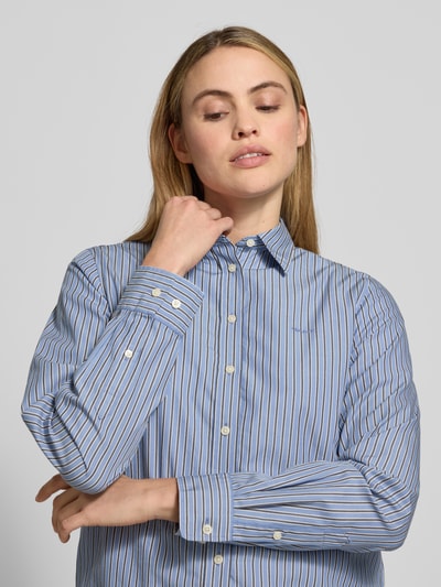 Frauenmodel trägt Regular Fit Bluse mit Label-Stitching von Gant aus reiner Baumwolle, blau mit weißen Streifen, Nahaufnahme Oberkörper.