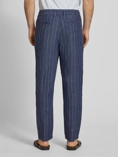 Männermodel trägt Leinenhose mit französischen Eingrifftaschen von MCNEAL, dunkelblau mit weißen Streifen, reines Leinen, Ganzkörperansicht Rückansicht. Straight Fit, elastischer Bund, Knopf- und Reißverschluss, Gesäßleistentaschen, rückseitiges Label-Stitching, Bundweite Größe M 43 cm, Innenbeinlänge 78 cm.