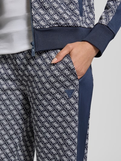 Frauenmodel trägt Wide Leg Sweatpants im Allover-Look Modell 'MAYA' von Guess Activewear mit elastischem Bund und gemustertem Stoff, Nahaufnahme Oberkörper.