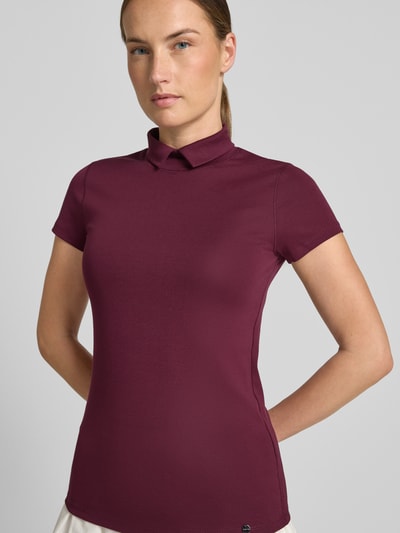 Frauenmodel trägt Slim Fit T-Shirt mit hochschließendem Polokragen von Marc Cain aus Baumwoll-Elasthan-Mix, Damen T-Shirt, 1/2-Arm, Rückenlänge bei Größe 36: 59 cm, satter Beerenfarbton, glatte Struktur, Ganzkörperansicht von vorne.