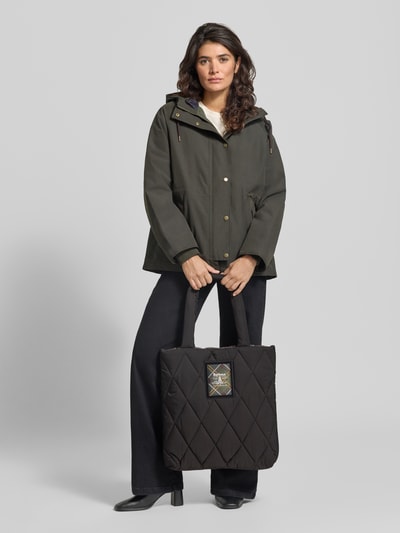 Frauenmodel trägt schwarze Henkeltasche mit Label-Patch von Barbour, Rautenmuster, glatte Textur, Ganzkörperansicht von vorne. Damen Henkeltasche von Barbour