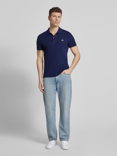 Męski model nosi Slim Fit Poloshirt aus reiner Baumwolle von Lacoste, jednolity, krój slim fit, logo, krótki rękaw, piqué, bawełna, widok całej sylwetki z przodu.