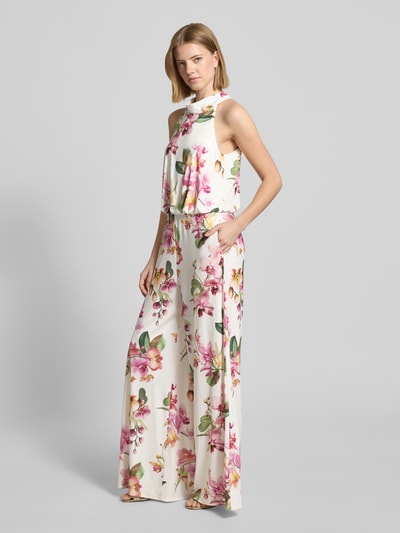 Modelka nosi Regular Fit Jumpsuit mit floralem Allover-Print von V by Vera Mont, białe tło z różowym kwiatowym wzorem, krój regular fit, bez rękawów, cut-out na plecach, zamek w szwie, długość pleców w rozmiarze 36: 147 cm, szerokość w rozmiarze 36: 36 cm, całkowita długość w rozmiarze 36: 132 cm, długość wewnętrzna nogawki w rozmiarze 36: 81 cm, całkowity widok z przodu