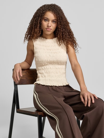 Modelka nosi Top mit Smok-Details und Rundhalsausschnitt von Jake*s Casual, mieszanka bawełny z dodatkiem streczu, dopasowany krój, okrągły dekolt, marszczone detale, długość tyłu w rozmiarze 38: 51 cm, jasny beż, szerokie spodnie, tło szare, Ganzkörperansicht z przodu.