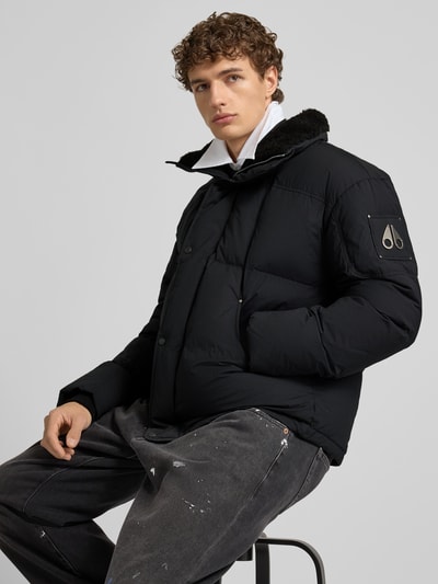 Männermodel trägt Steppjacke mit Stehkragen van Moose Knuckles, regular fit, verborgen ritssluiting, steekzakken, zwart, detailopname bovenlichaam.