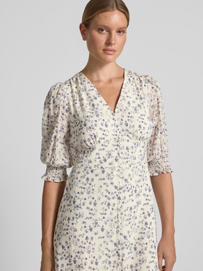 Frauenmodel trägt Midikleid mit floralem Allover-Print Modell 'Valley' von Neo Noir in Creme mit blauen Blumenmotiven, Nahaufnahme Oberkörper. Taillierte Passform, V-Ausschnitt, Halbarm, florale Textur.