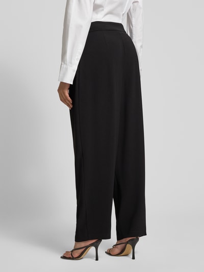 Frauenmodel trägt Relaxed Fit Hose mit Bundfalten von ARMANI EXCHANGE, schwarz mit Eingrifftaschen, glatte Textur, Ganzkörperansicht Rückansicht.