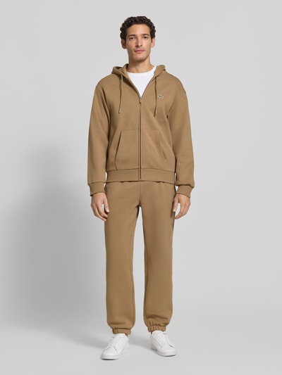 Männermodel trägt Regular Fit Sweatjacke aus Baumwoll-Mix von Lacoste in Hellbraun mit glatter Textur, Ganzkörperansicht von vorne. Herren Sweatjacke von Lacoste