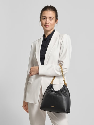 Kobiece model prezentuje czarną torbę na ramię 'Schultertasche mit Label-Details Modell 'INDIE' von MICHAEL Michael Kors z logo, pasek na ramię z efektem łańcuszka, główna przegroda z zapięciem na zatrzask, szerokość w rozmiarze 1: 27 cm, długość w rozmiarze 1: 24 cm, głębokość w rozmiarze 1: 10 cm, długość paska na ramię w rozmiarze 1: 42 cm, widok na cały korpus z przodu.